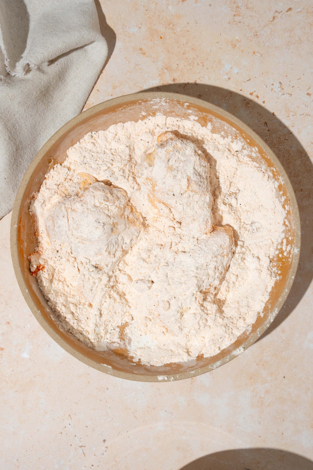 A plate with cornstarch seasoning mixture with chicken wings coated in the mixture. The plate is on a tan counter with a white cloth napkin.