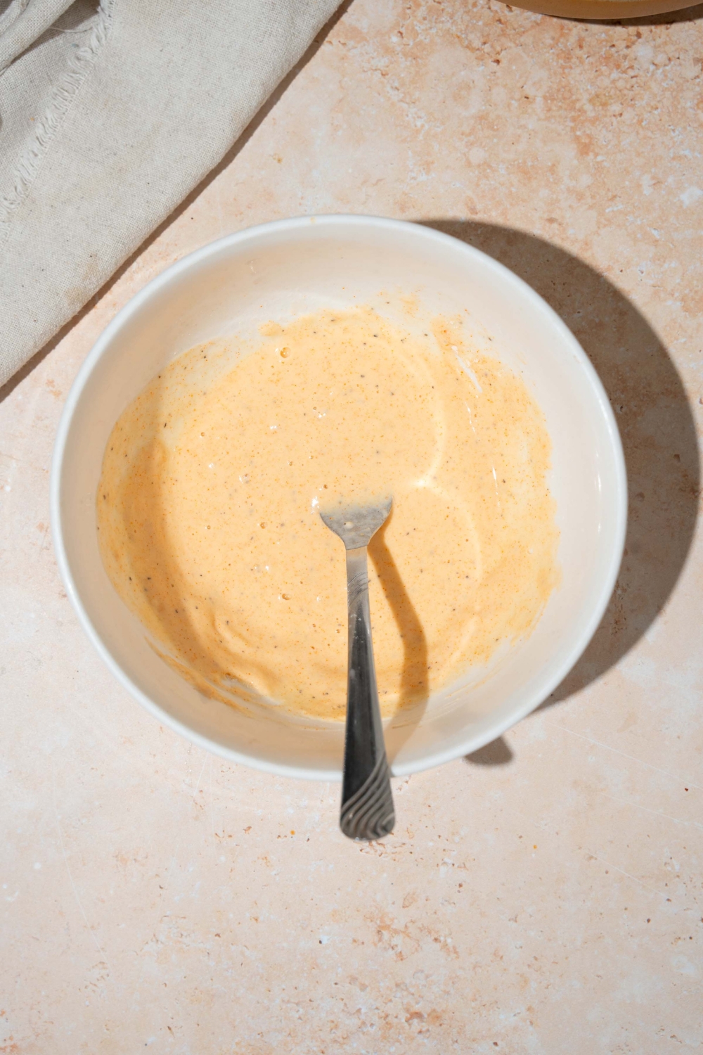 A white bowl with a fork mixing seasoning and water mixture. The bowl is on a tan counter.