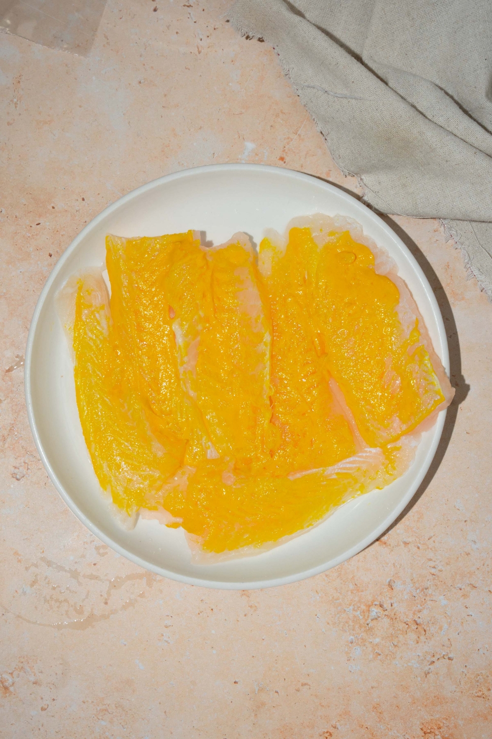 A white plate with fresh whiting coated in mustard. The plate is on a tan counter.