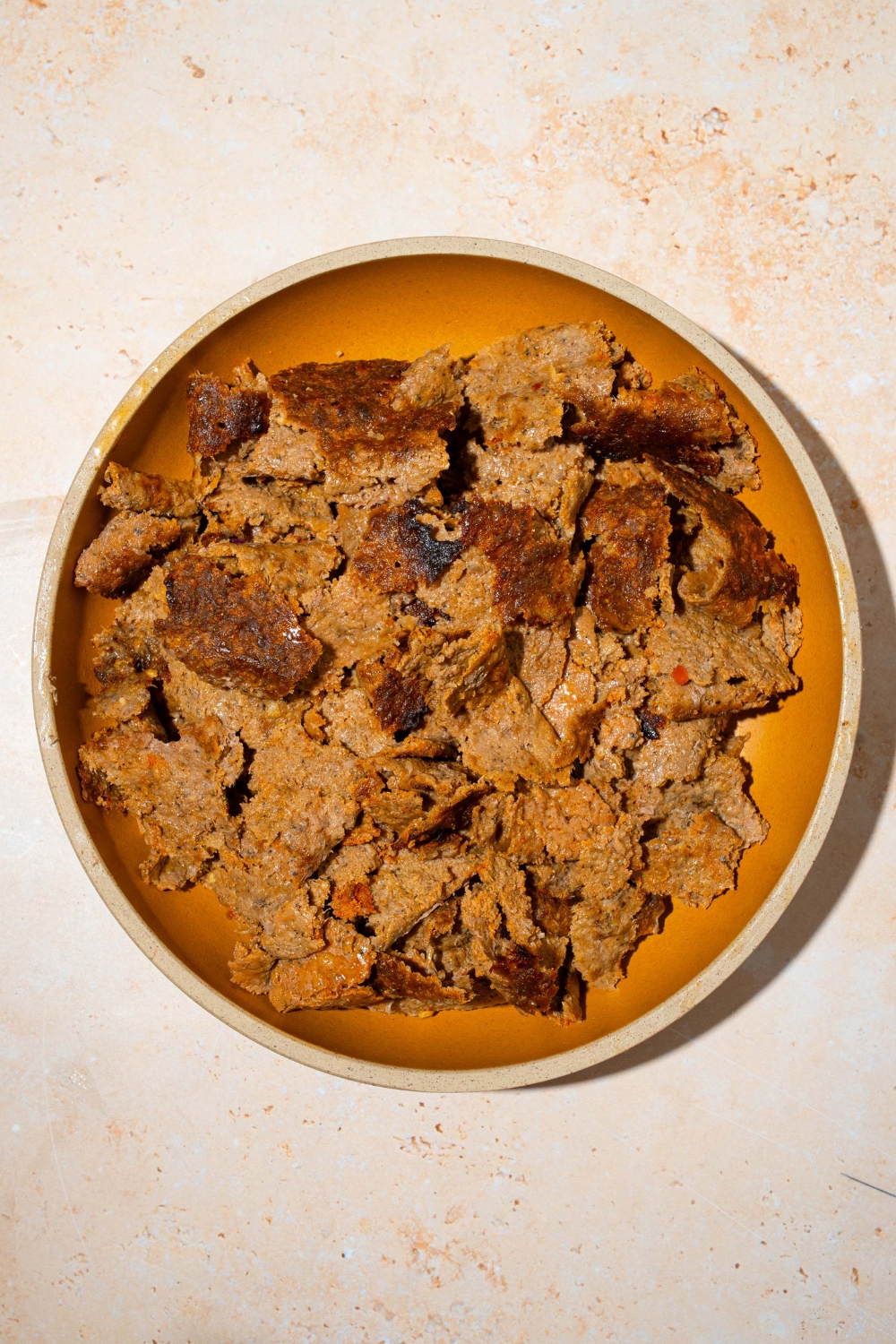 A plate with shredded doner kebab meat. The plate is on a tan counter.