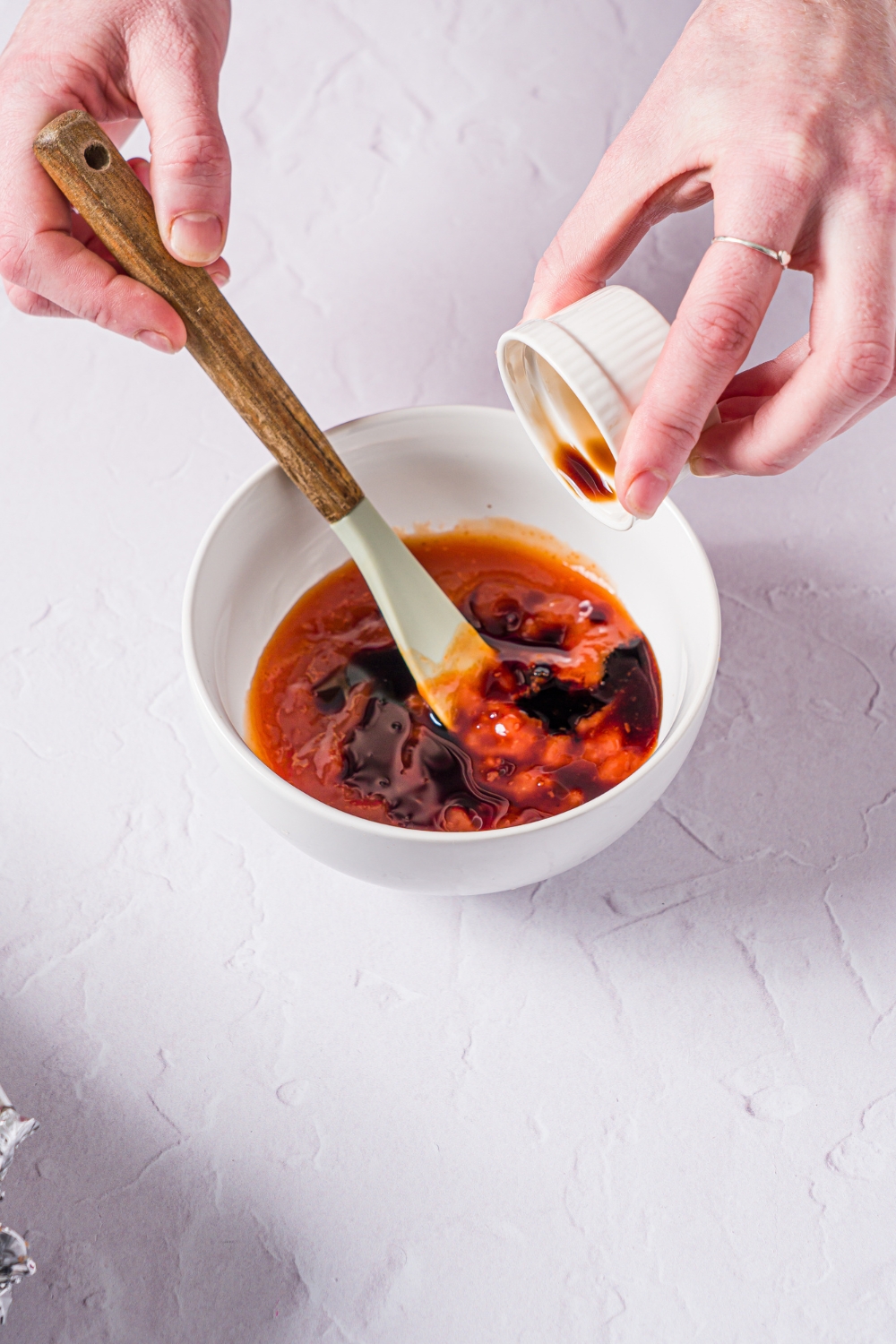 A small white bowl with a spatula mixing ingredients for a meatloaf glaze including ketchup and Worcestershire sauce. The bowl is on a marble counter.