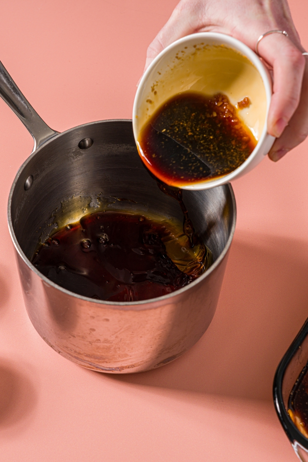 A sauce pan with a bowl of marinade being poured into the pan. The pan is on a pink counter.