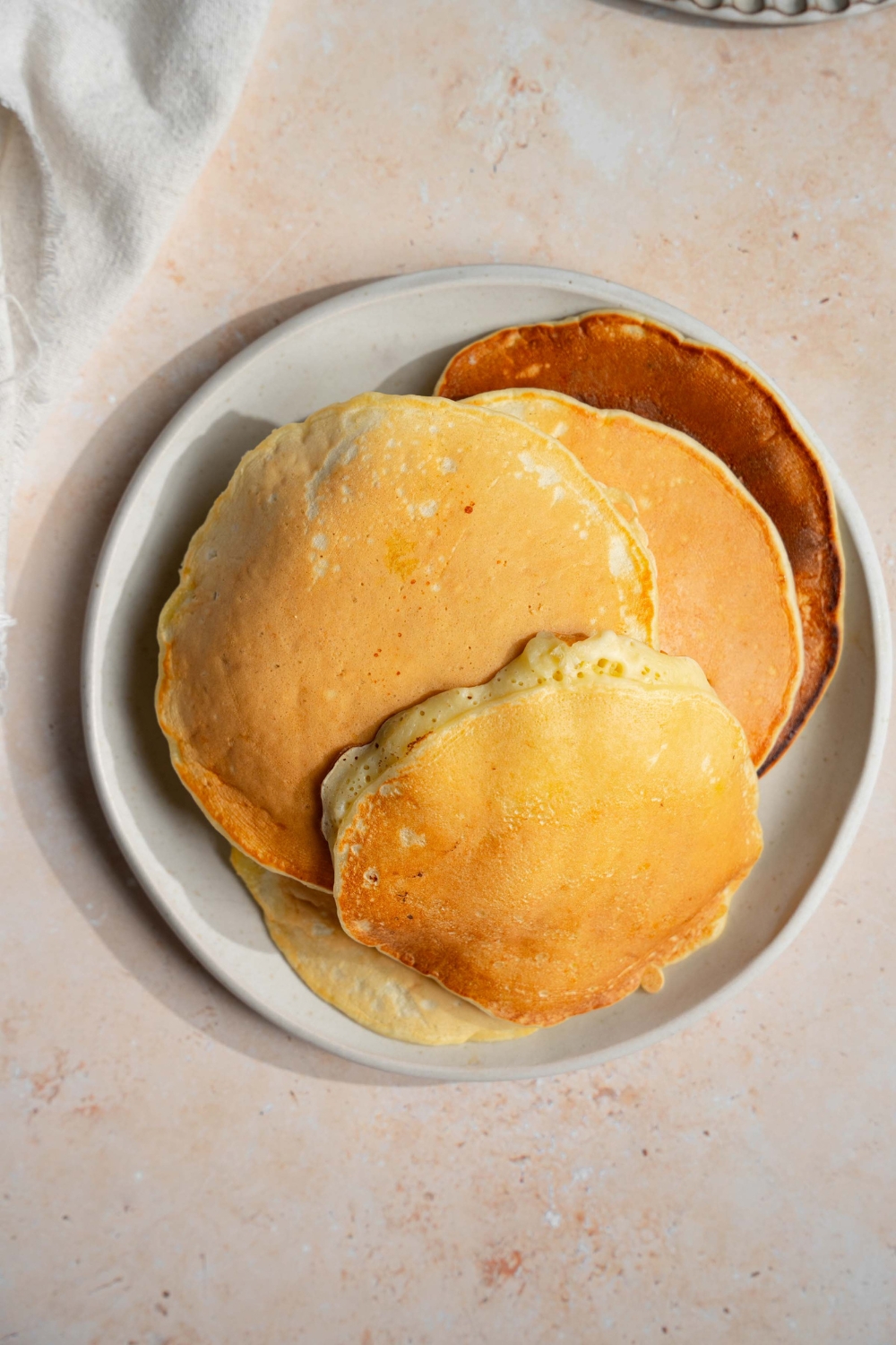 A white plate with a pile of banana pancakes. The plate is on a tan counter.
