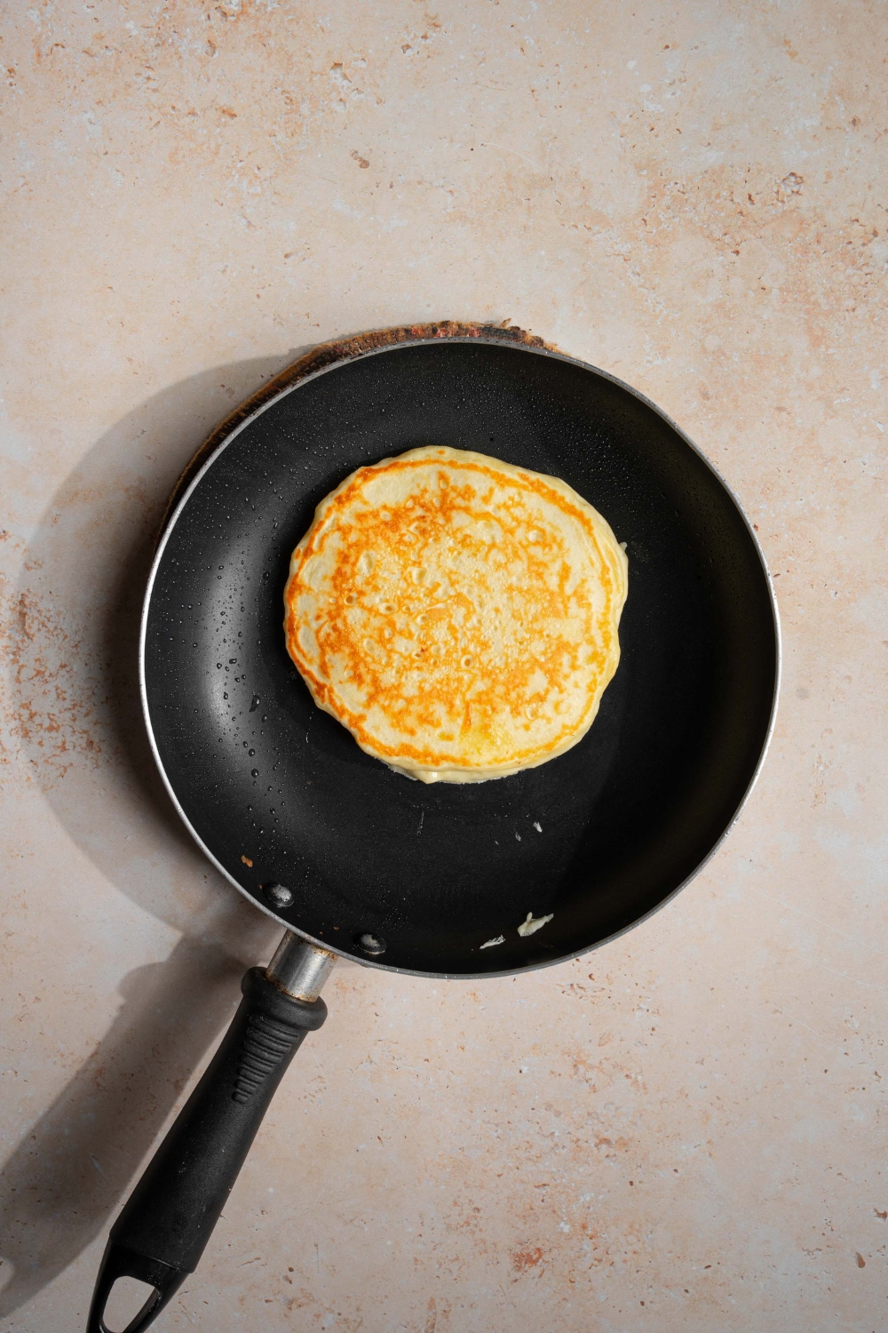 A skillet with a flipped banana pancake. The skillet is on a tan counter.