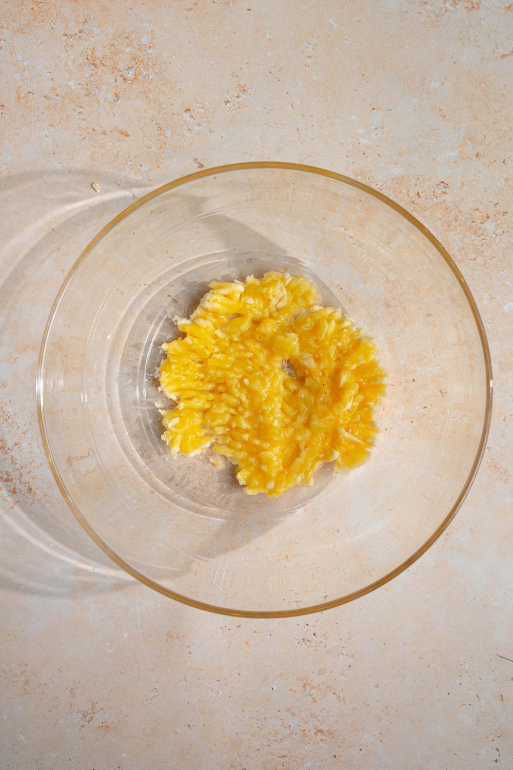 A glass bowl with mashed bananas. The bowl is on a tan counter.