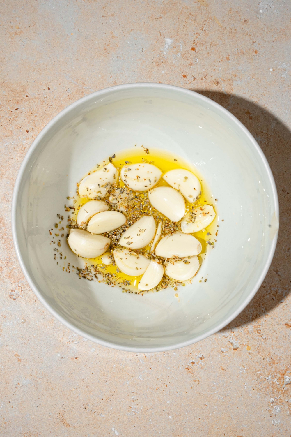 A white bowl with fresh garlic in oil and seasonings. The bowl is on a tan counter.