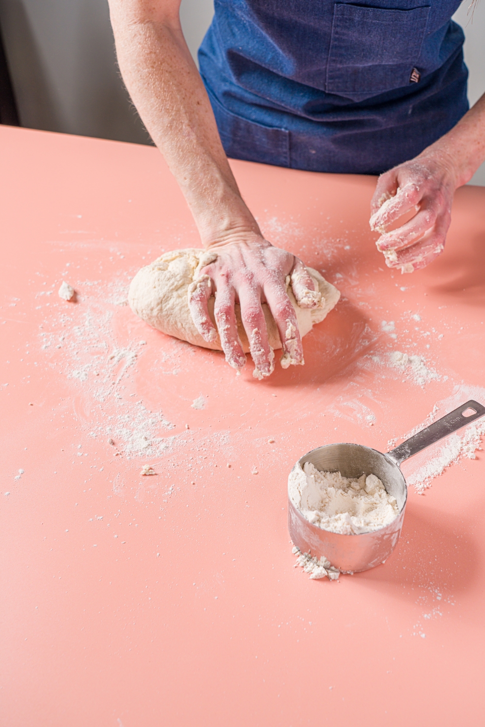 A pink counter with a pair of hands kneading greek yogurt bagel dough.