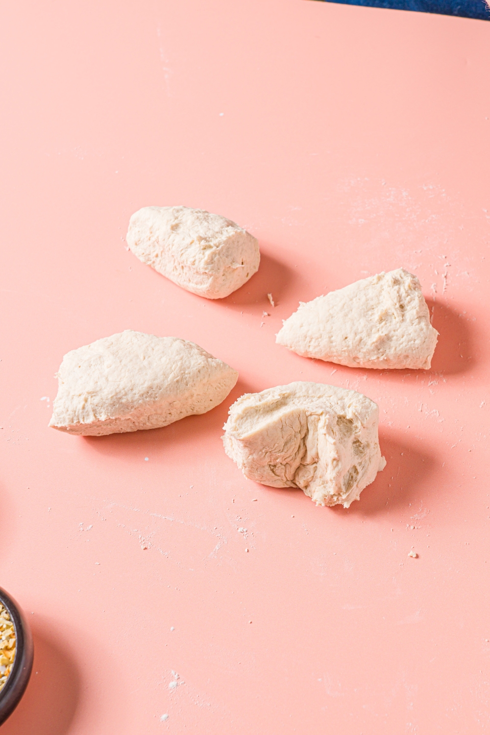 A pink counter with several chunks of greek yogurt bagel dough.
