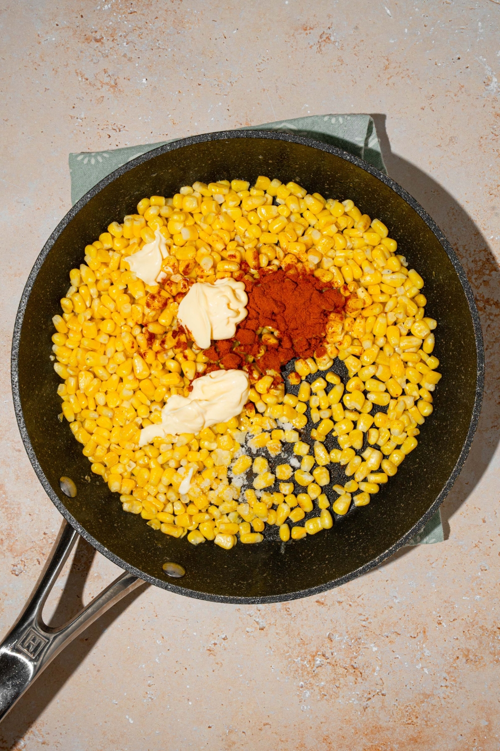 A skillet with corn cooked topped with butter, mayo, and seasonings. The skillet is on a tan counter.
