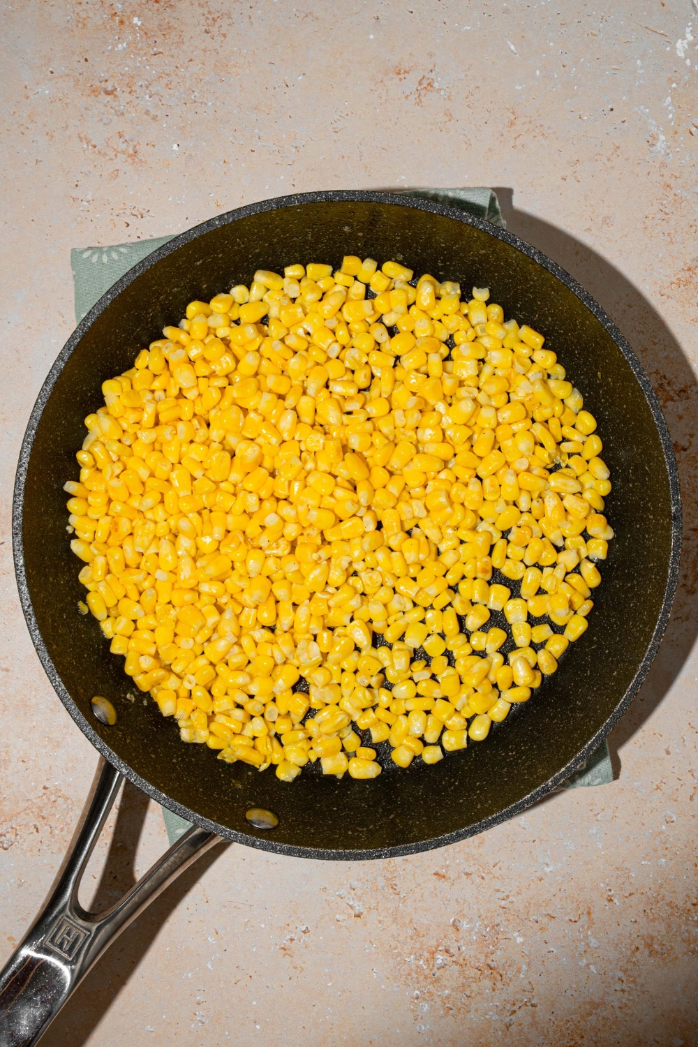 A skillet with corn. The skillet is on a tan counter.
