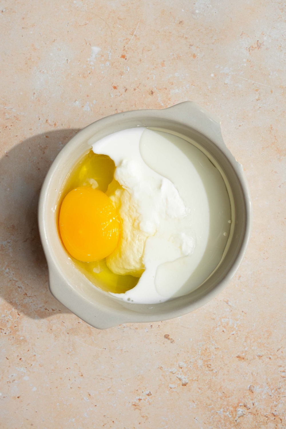 A white bowl with wet ingredients to make pancakes including egg and milk. The bowl is on a tan counter.