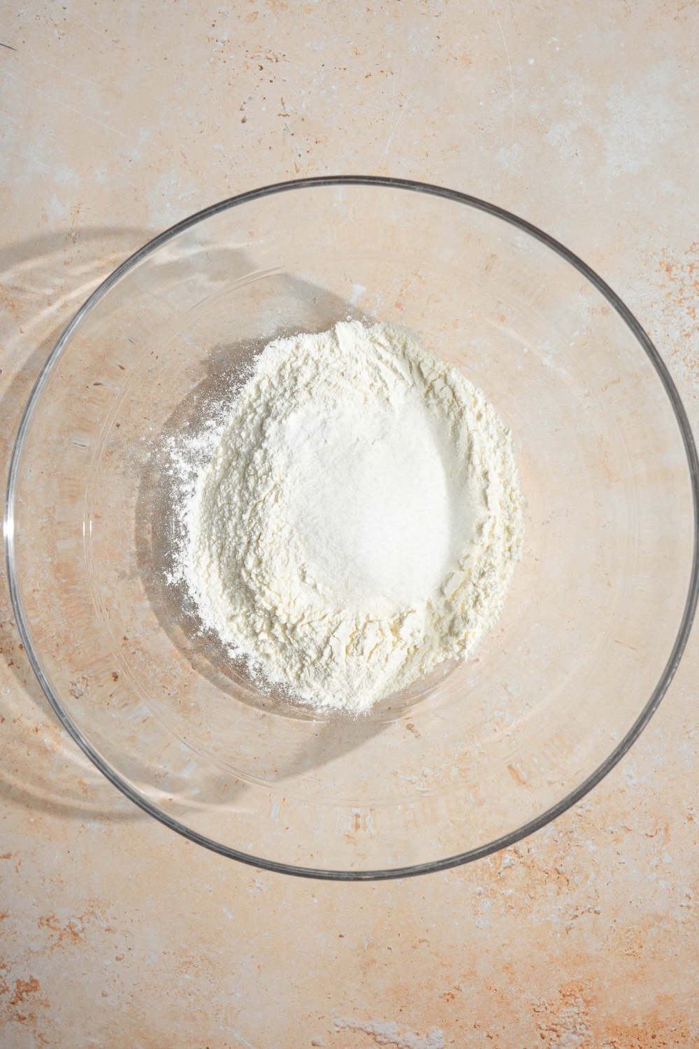 A large glass bowl with ingredients to make pancakes including self rising flour, sugar, and baking soda.