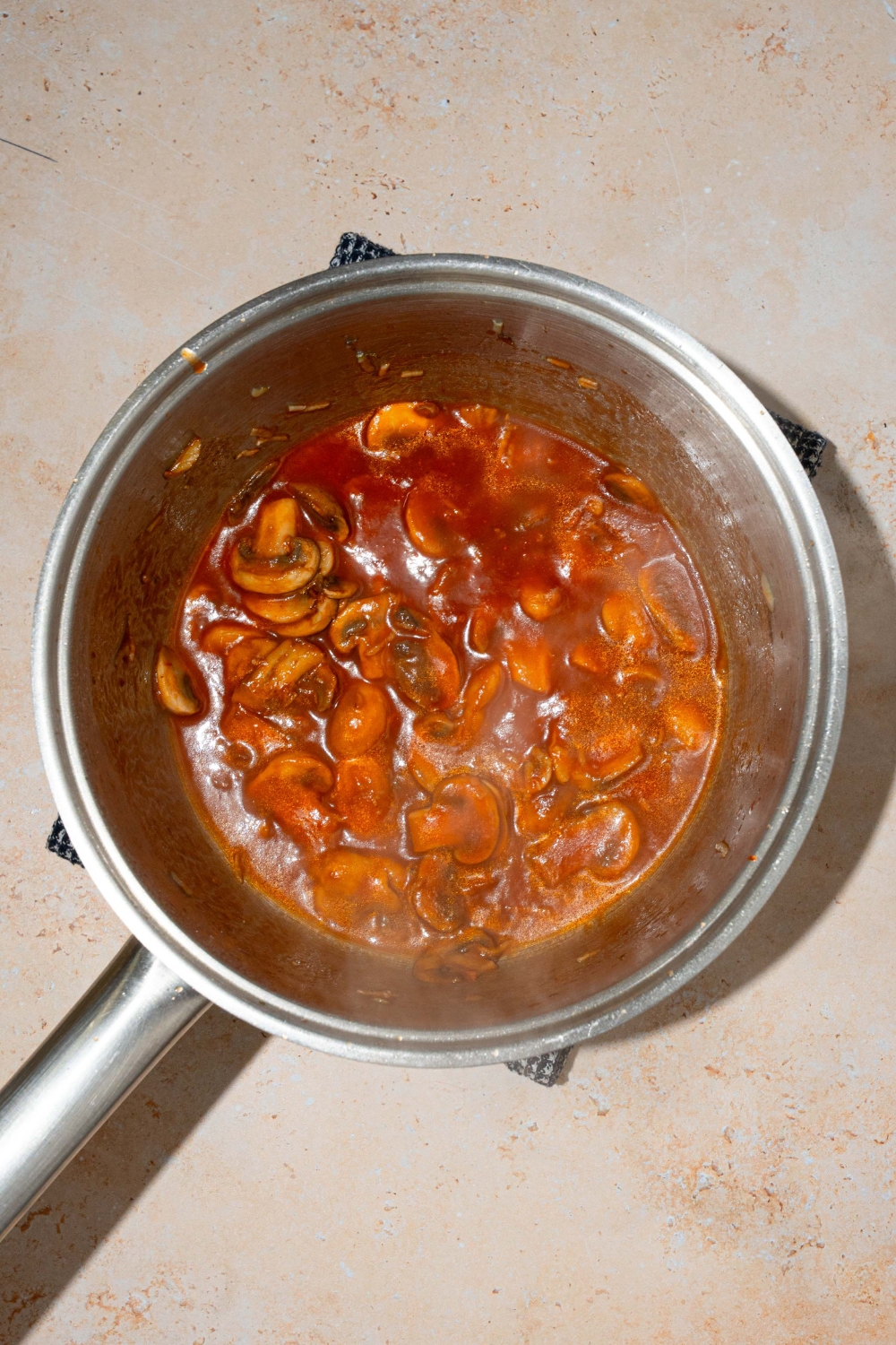 A pot with sautéed mushrooms cooking in marinara sauce. The pot is on a tan counter.