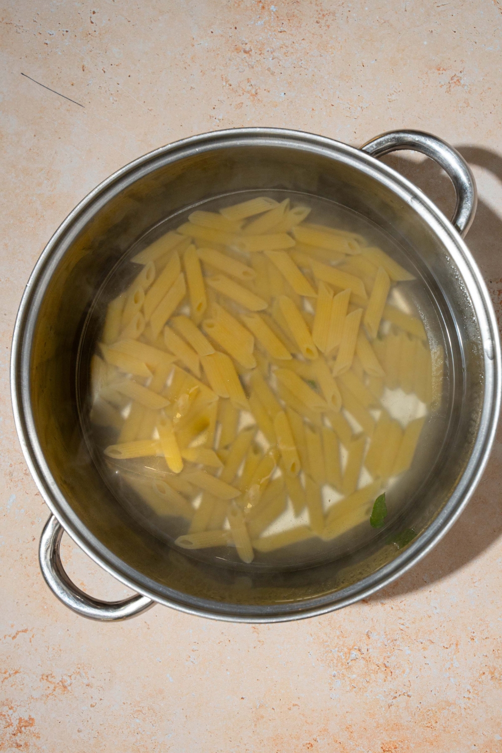 A pot with penne pasta cooking in water. The pot is on a tan counter.