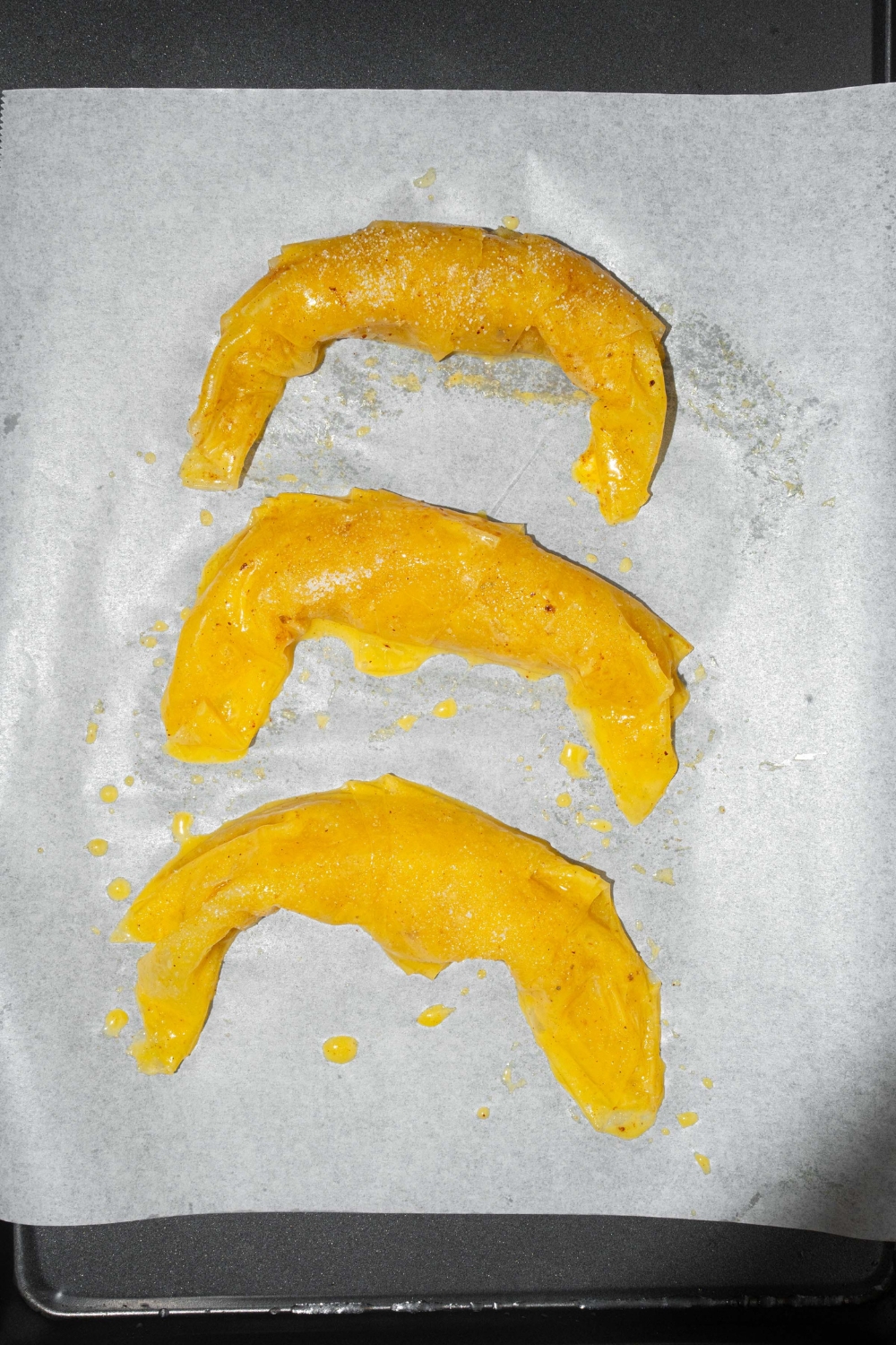 A baking sheet lined with parchment paper with three unbaked rolled rice paper croissants.
