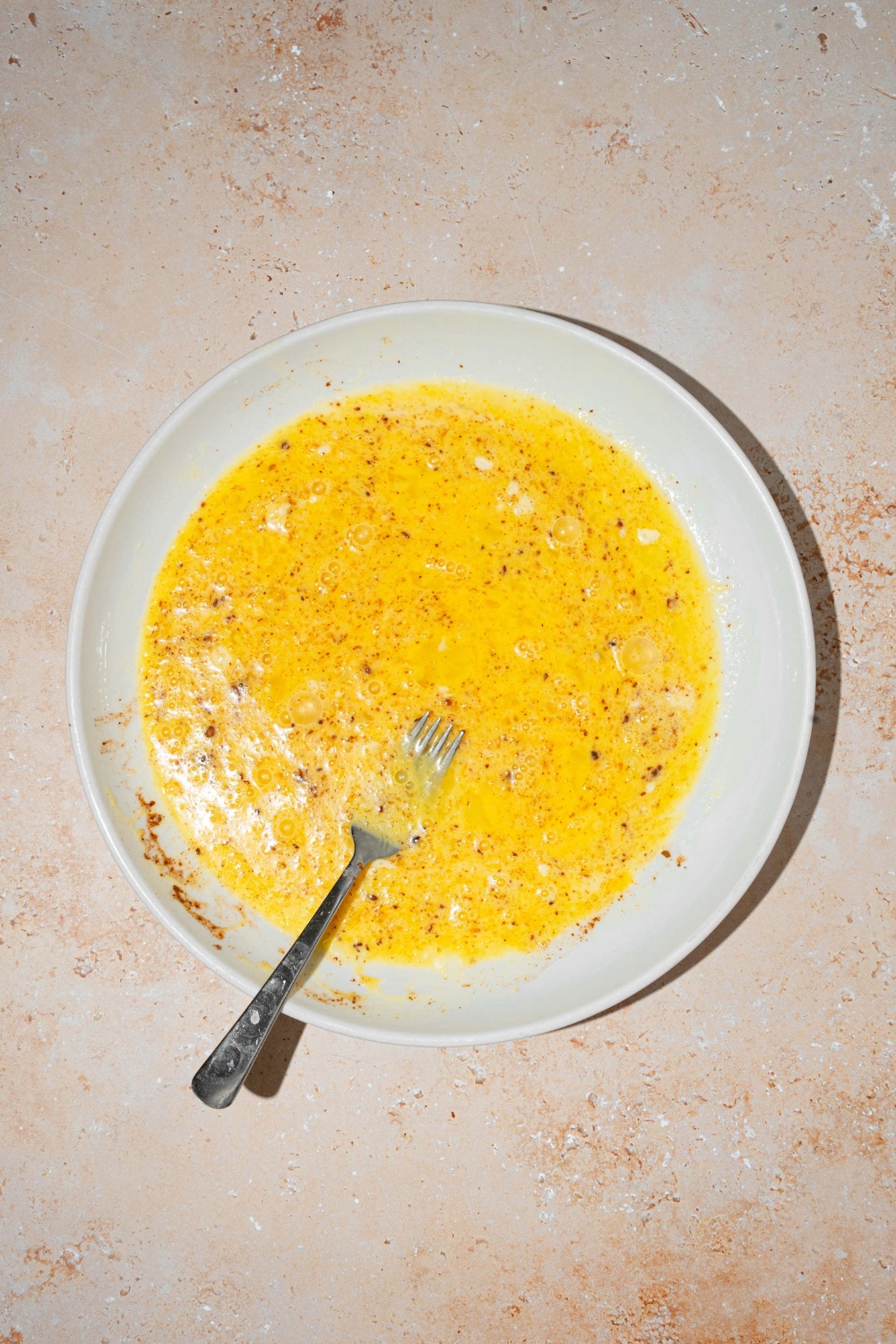 A white plate with a fork mixing an egg custard mixture. The plate is on a tan counter.