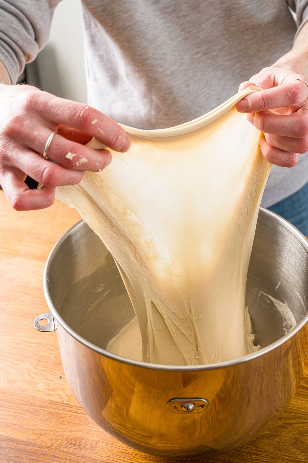 A mixing bowl with salt bread dough being stretched. The bowl is on a wooden counter.