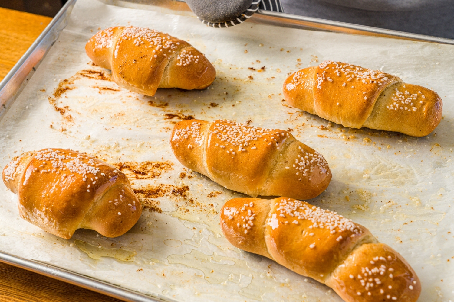 A baking sheet lined with parchment paper with baked pieces of salt bread. The sheet is on a wooden counter.