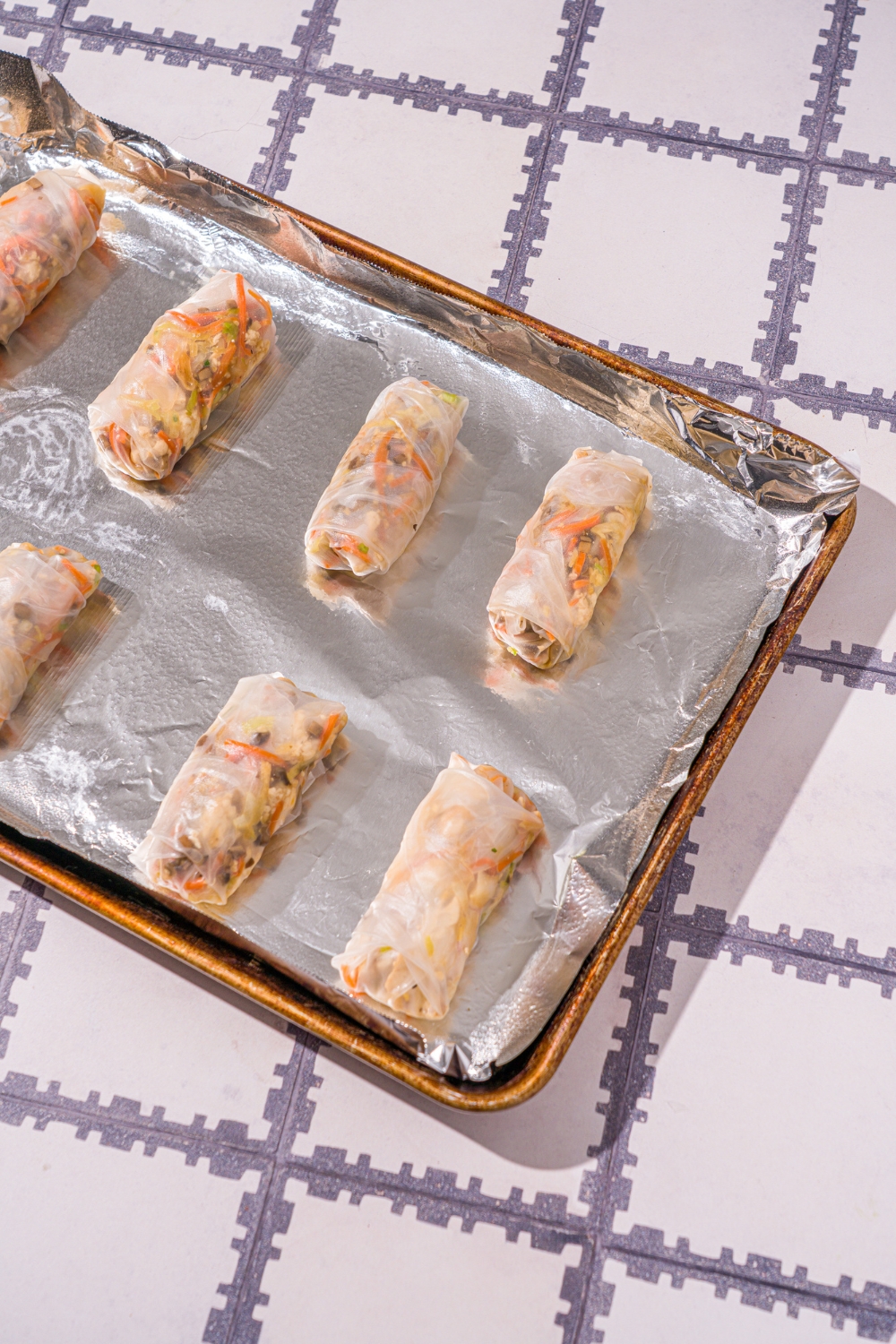 A baking sheet lined with foil with several rice paper veggie dumplings. The sheet is on a tiled counter.