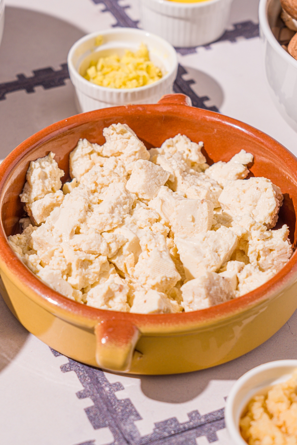 A small bowl with crumbled tofu. The bowl is on a tiled counter with small bowls of ingredients.