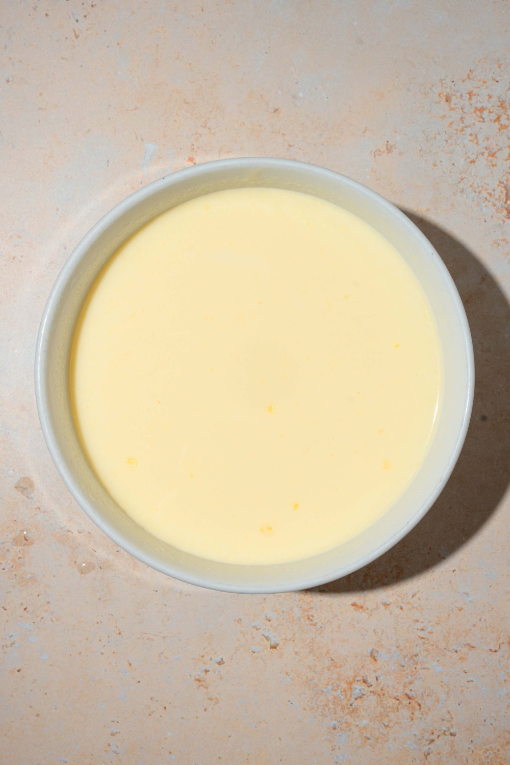 A white bowl with vanilla pudding. The bowl is on a tan counter.