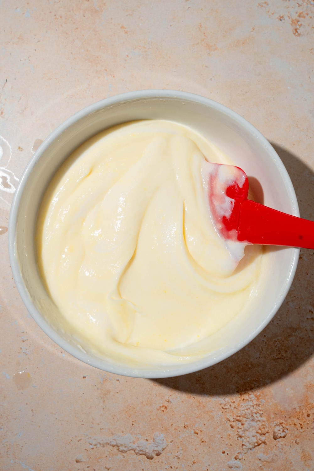 A white bowl with a spatula mixing vanilla pudding and whipped cream. The bowl is on a tan counter.
