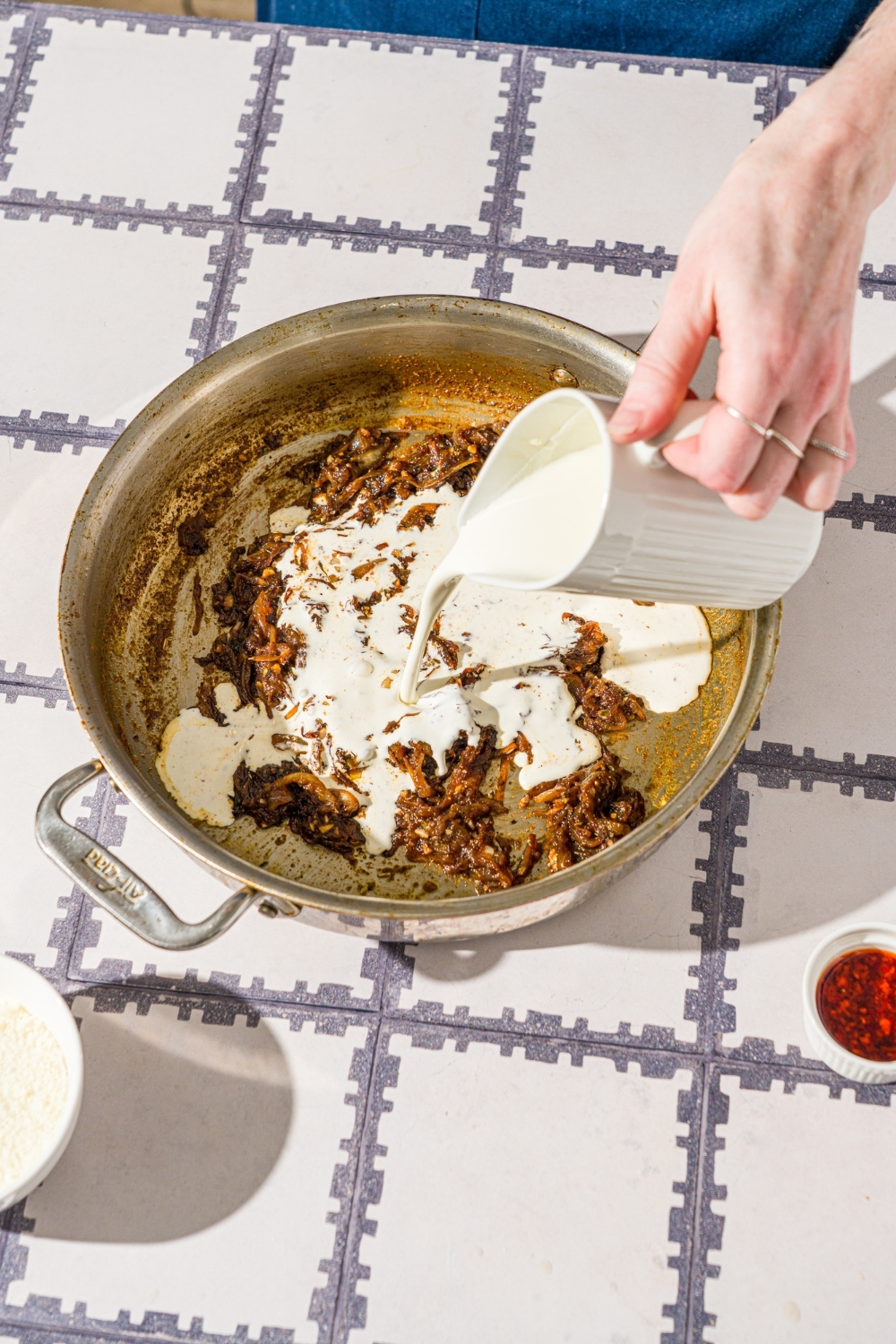 A skillet with heavy cream being added to caramelized onion. The skillet is on a tiled counter.