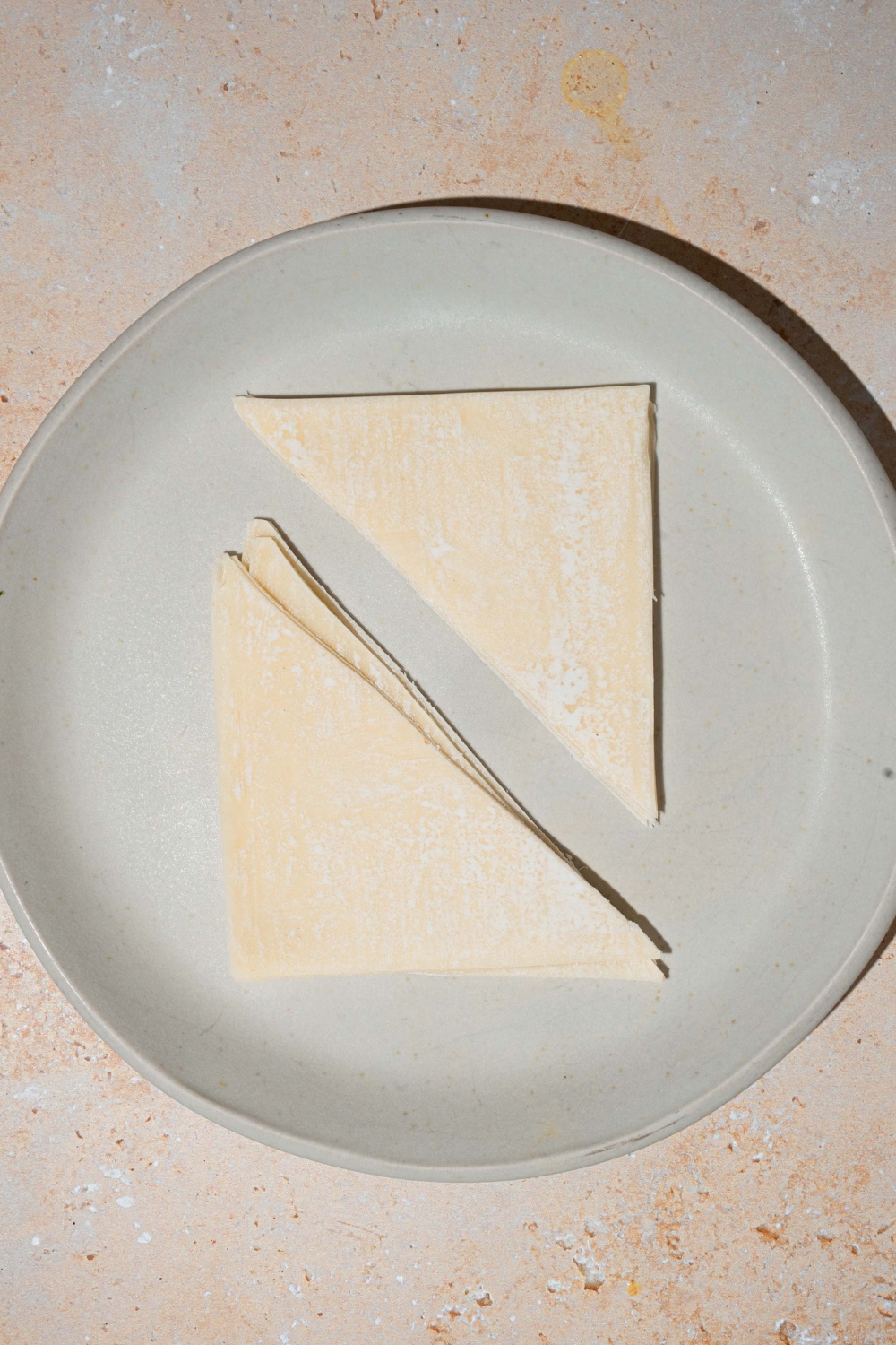 A white plate with wonton wrappers sliced diagonally. The plate is on a tan counter.