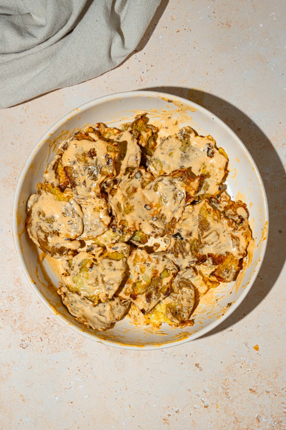 A white plate with crispy smashed potato salad tossed with chili crisp tahini dressing. The plate is on a tan counter.