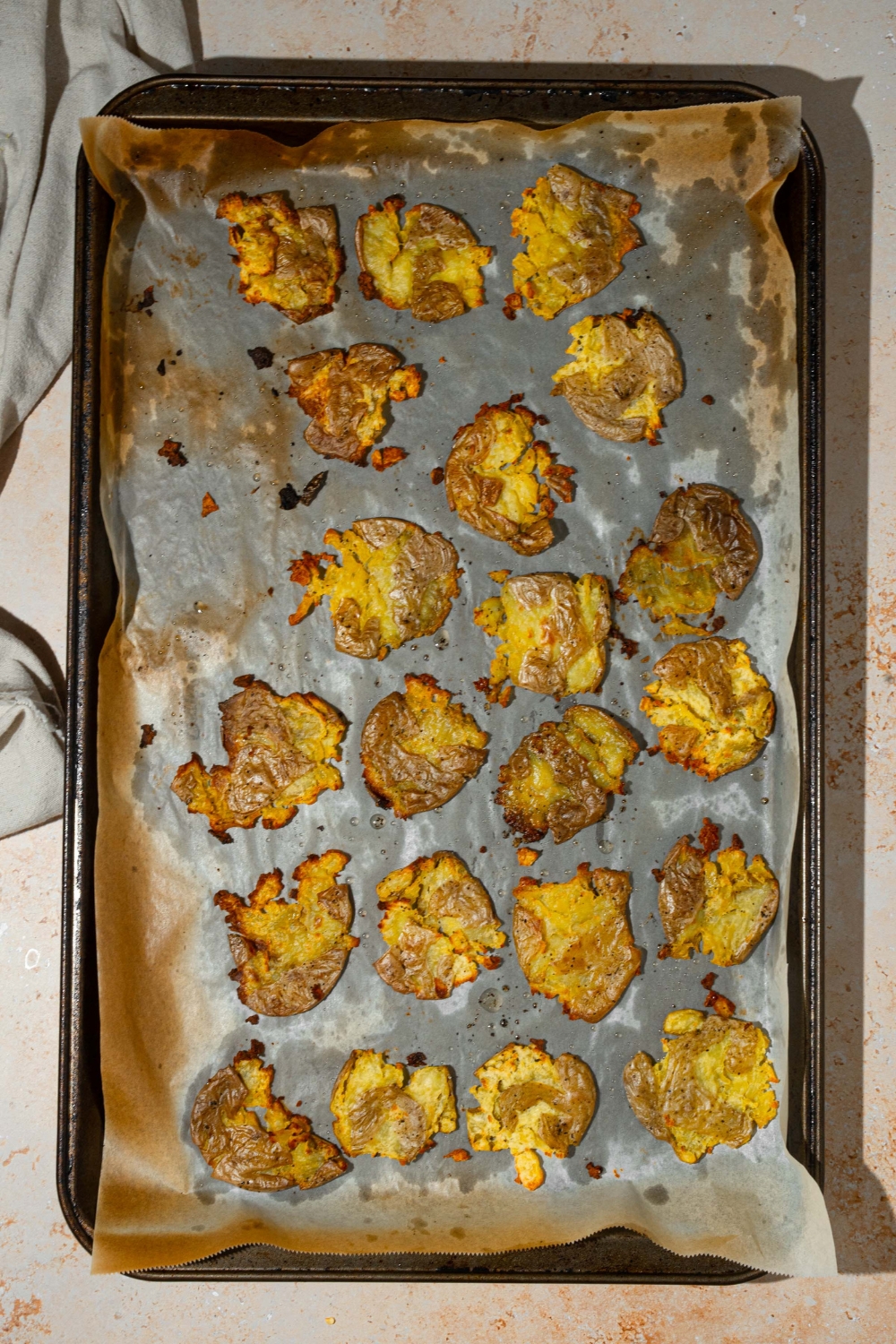A baking sheet lined with parchment paper with smashed baked baby potatoes. The sheet is on a tan counter.