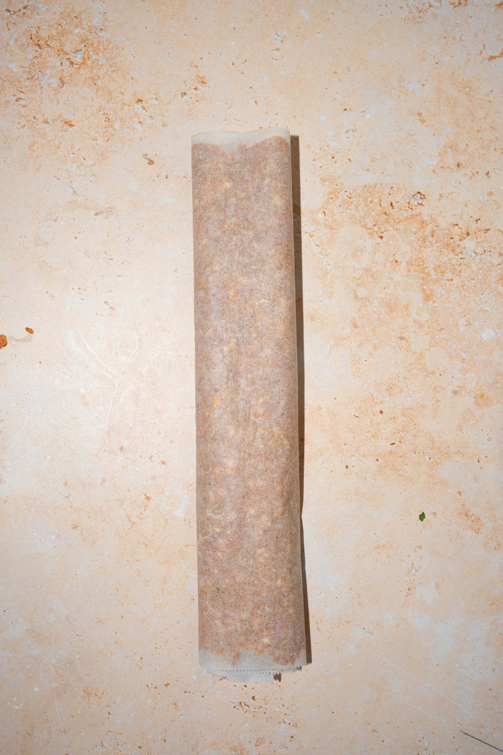 A ground beef mixture wrapped in a log with parchment paper. The log is on a tan counter.