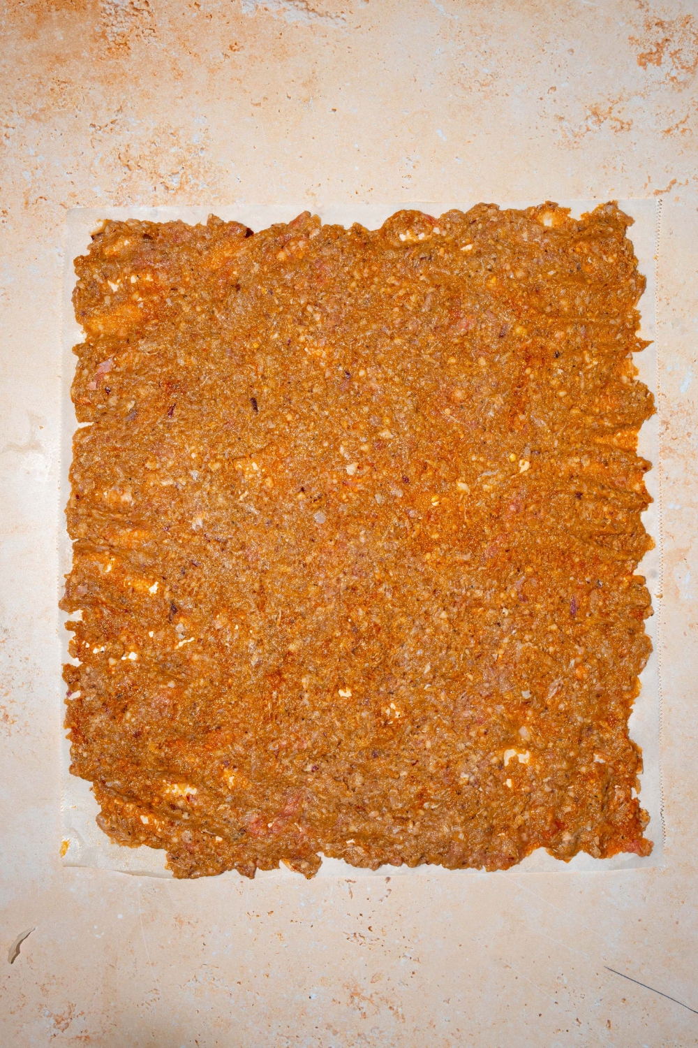 A ground beef mixture rolled into a square shape over a slice of parchment paper.