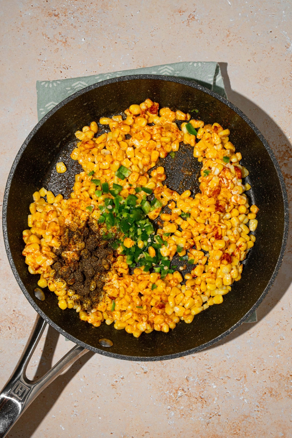 A skillet with seasoned corn with jalapeños, cream cheese, and shredded cheese. The skillet is on a tan counter.
