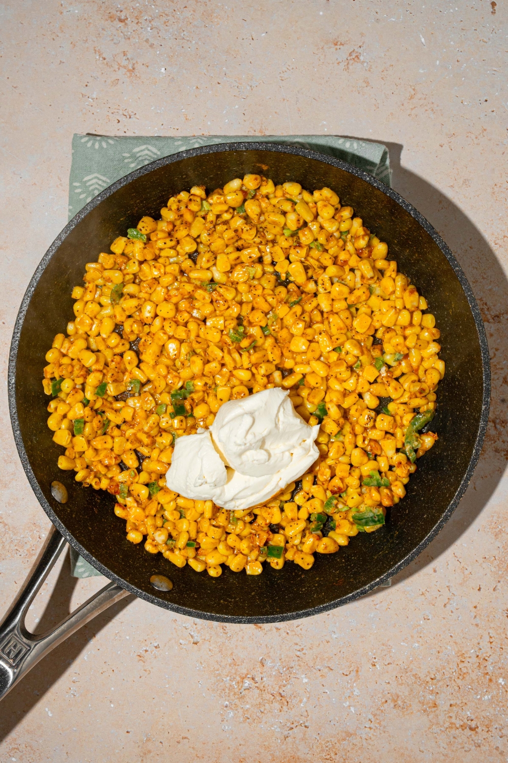 A skillet with seasoned corn topped with cream cheese. The skillet is on a tan counter.