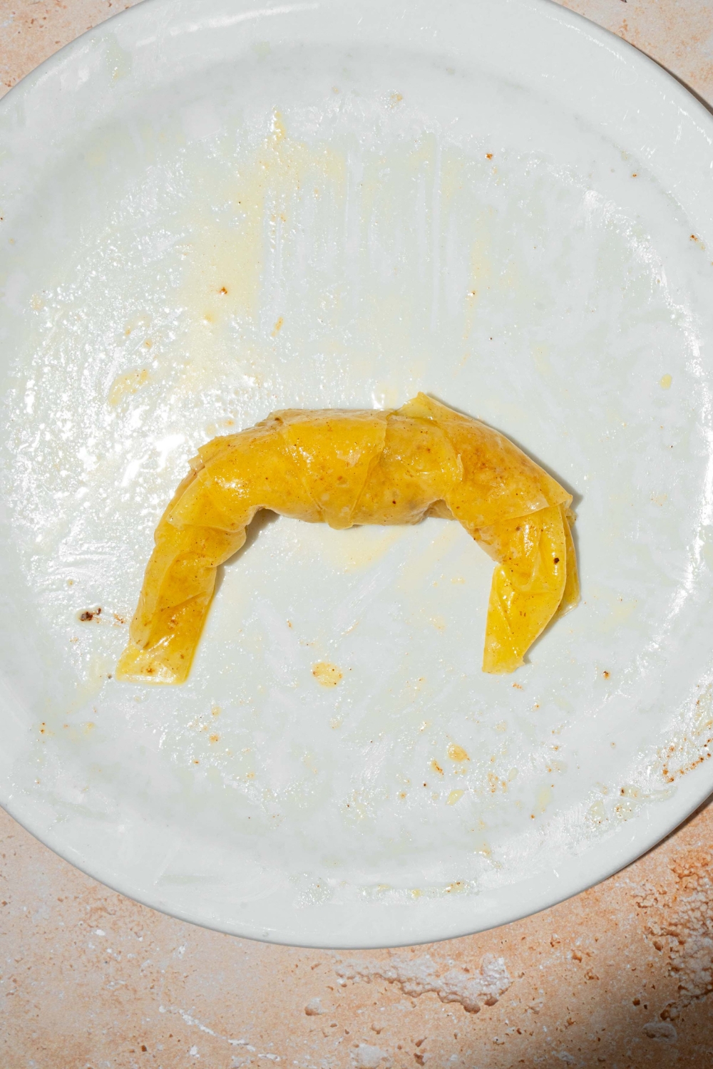 A plate with a rice paper soaked in egg custard rolled into a croissant. The plate is on a tan counter.