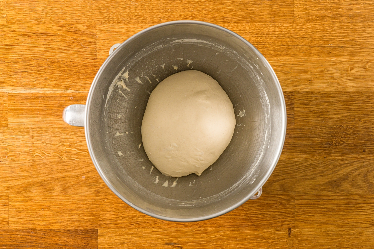 A mixing bowl with a ball of salt bread dough rising in the bowl. The bowl is on a wooden counter.
