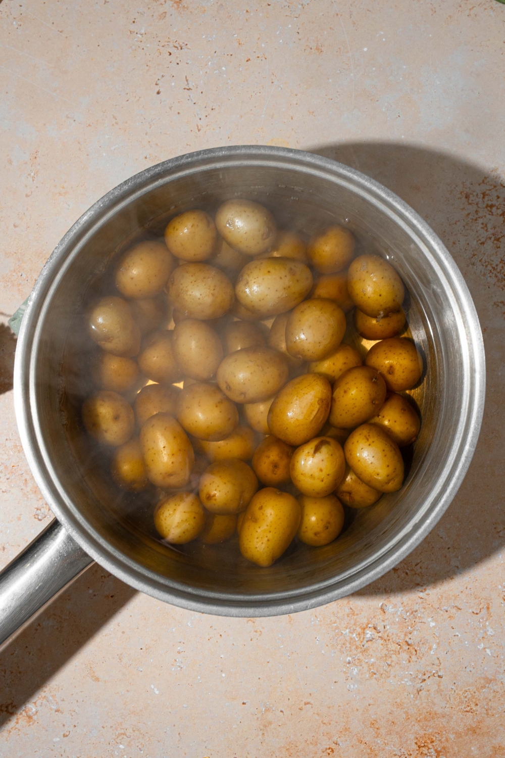 A steaming pot of baby potatoes with water. The pot is on a tan counter.