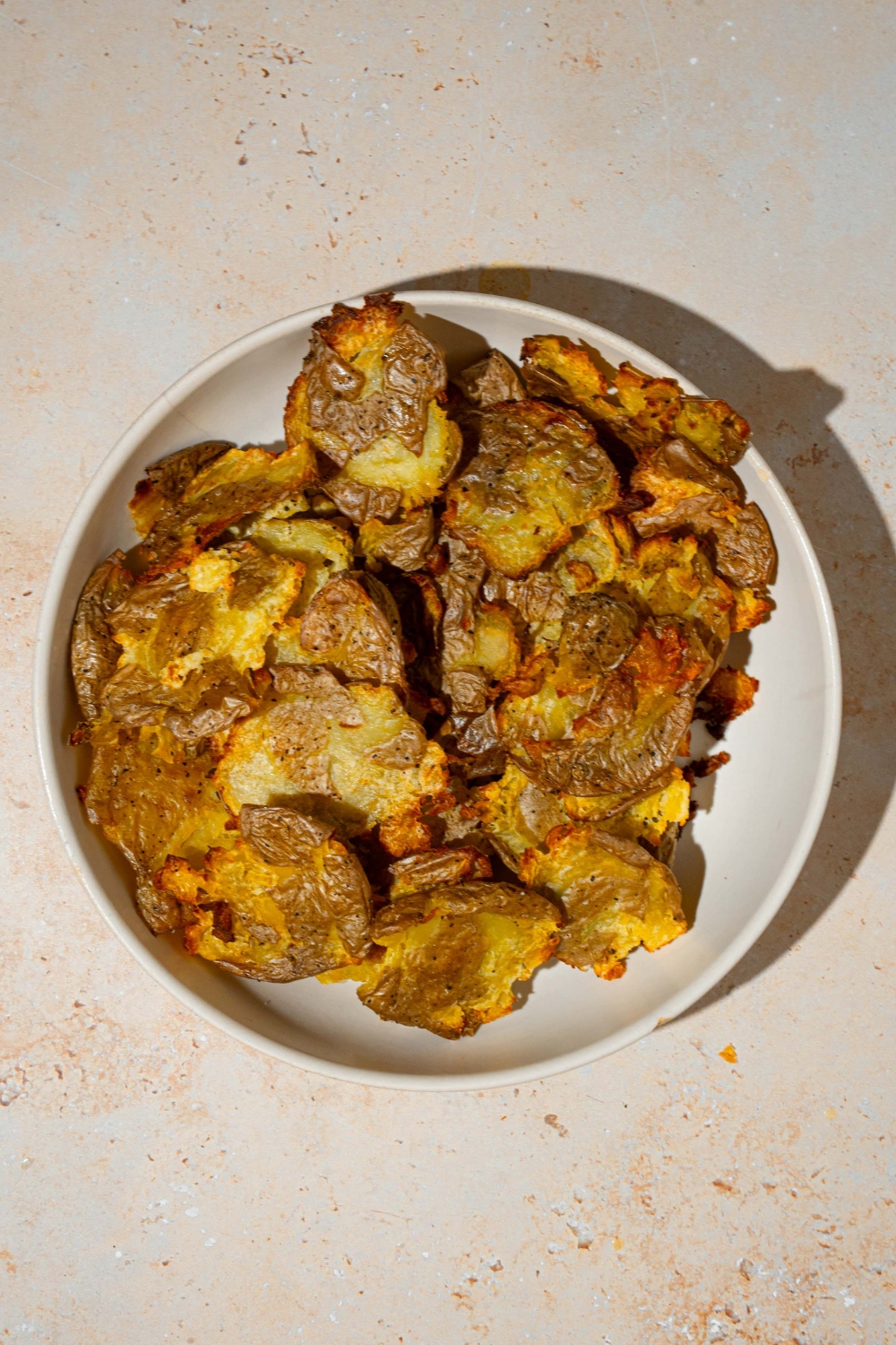 A white plate with crispy smashed baby potatoes. The plate is on a tan counter.