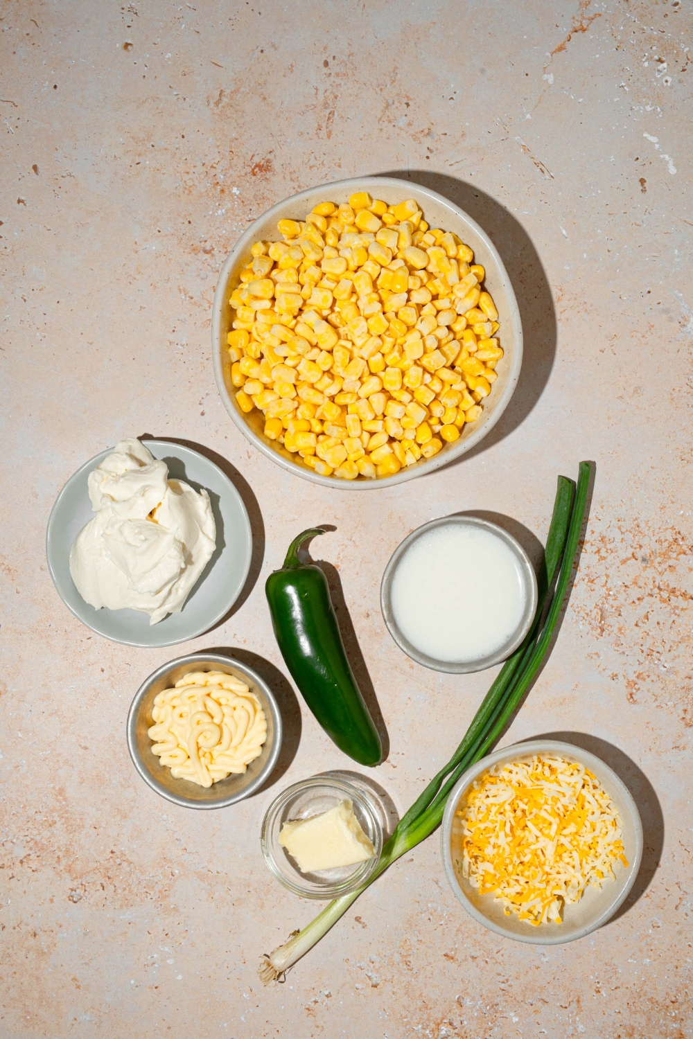 An overhead shot of several bowls in various sizes containing ingredients to make jalapeño corn dip including corn, mayo, cream cheese, shredded cheese, butter, jalapeño, and cream.