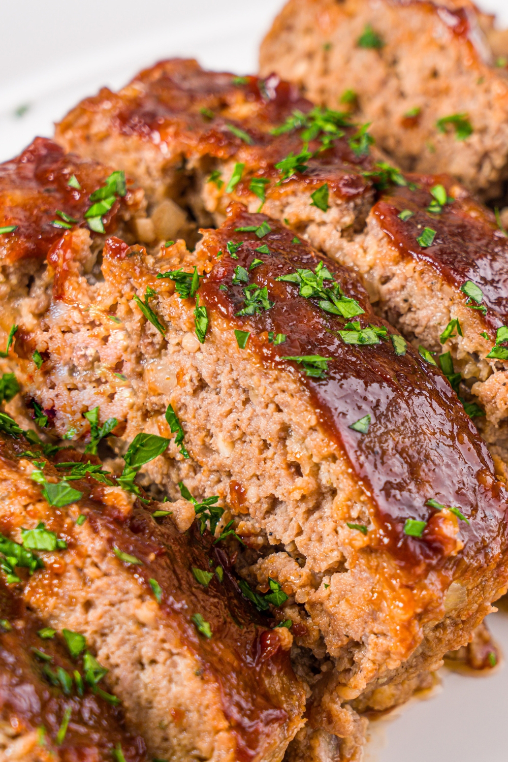 A white platter with sliced meatloaf topped with glaze and garnished with fresh parsley.