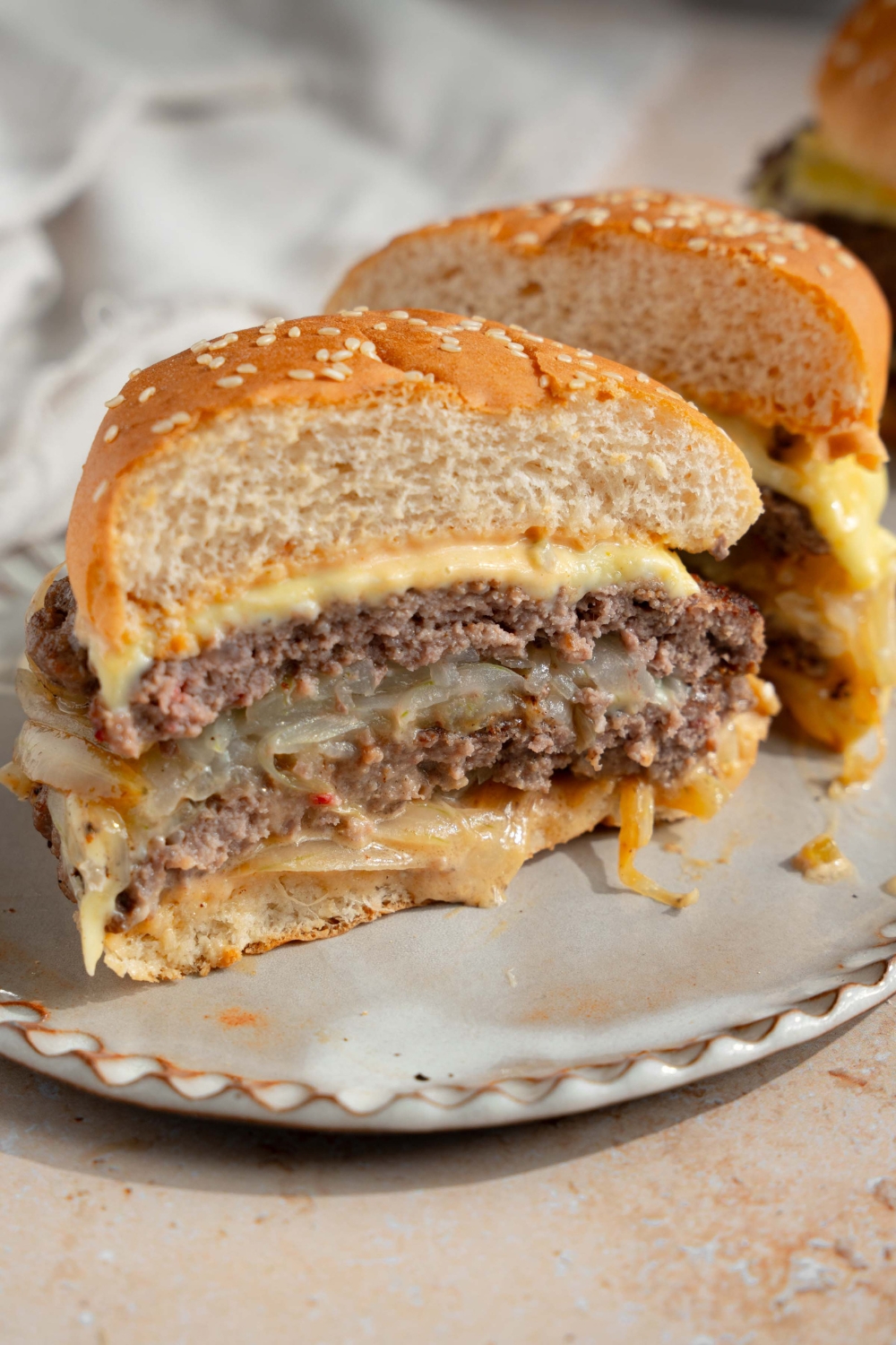 A white plate with a smash burger with onions sliced in half. The plate is on a tan counter.
