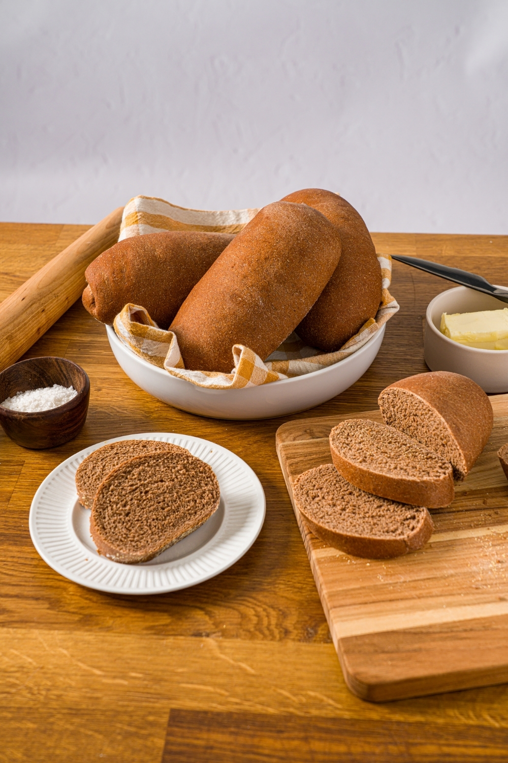 A white plate with two slices of Outback sweet molasses brown bread. The plate is on a wooden counter with a bowl of loaves and a cutting board with additional slices of bread.