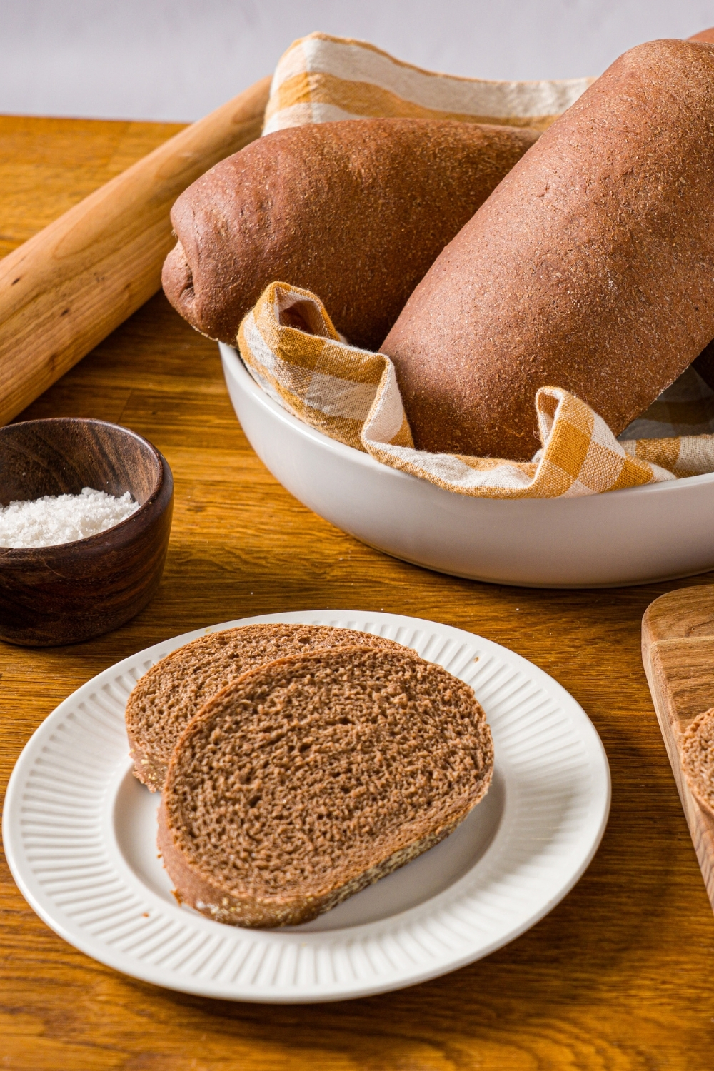 A white plate with two slices of Outback sweet molasses brown bread. The plate is on a wooden counter with a bowl of loaves.