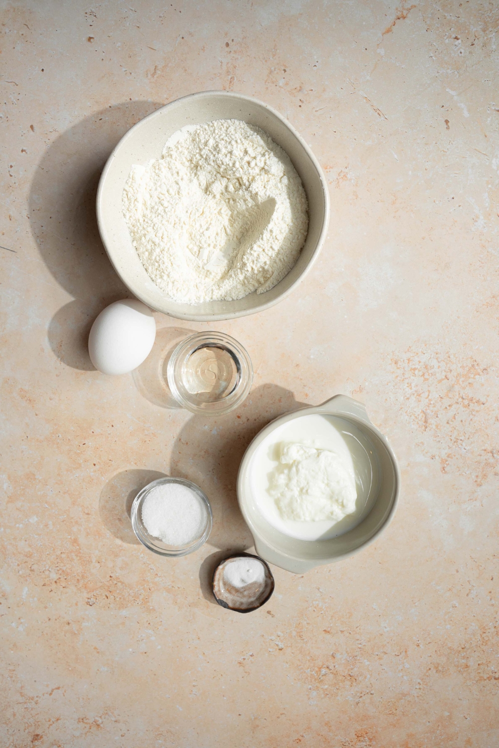 An overhead shot of several bowls in various sizes containing ingredients to make pancakes with self rising flour including self rising flour, sugar, baking soda, milk, and eggs.