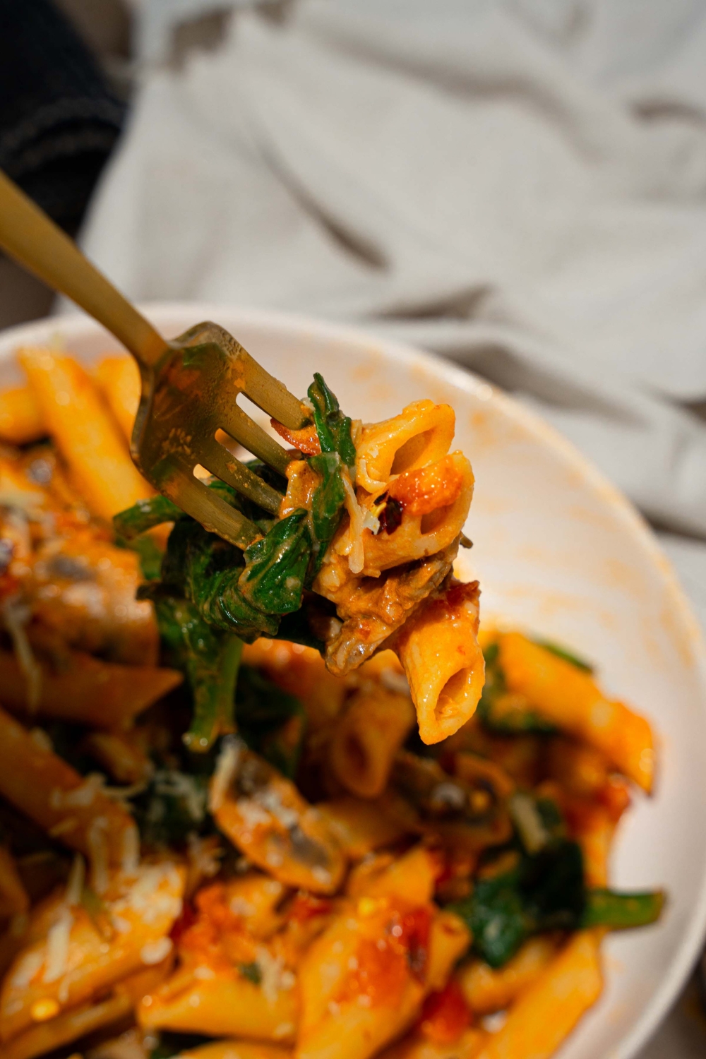 A close up of a fork with a bite of penne rosa with a bowl of penne rosa blurred in the background.