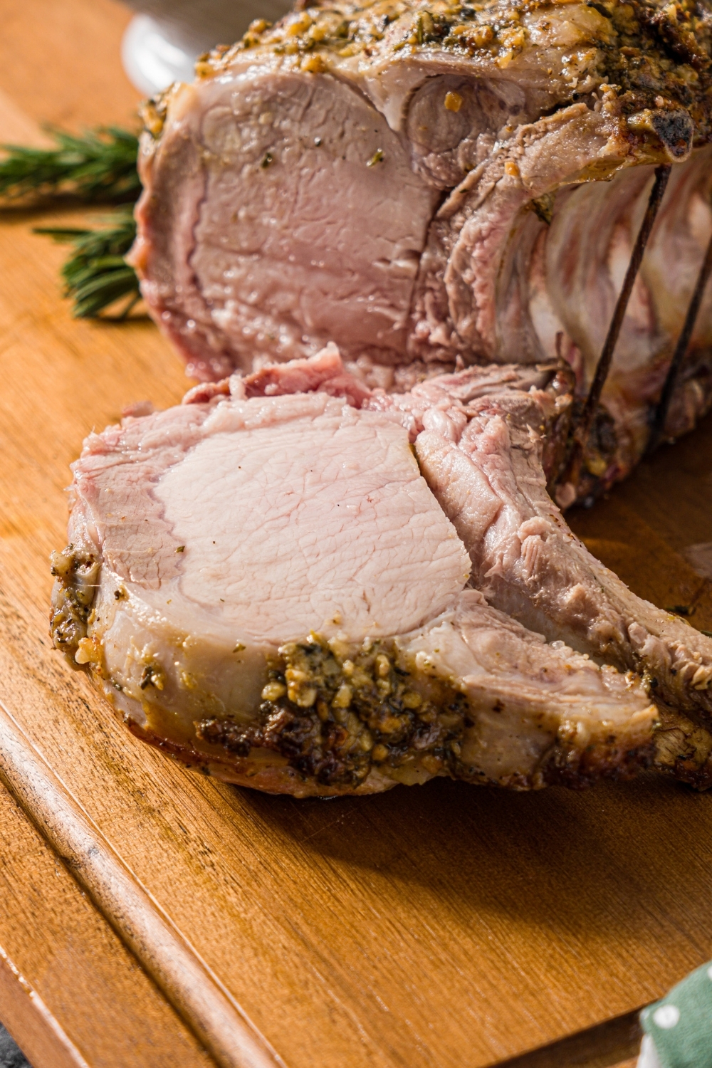 A wooden cutting board with a whole rack of pork topped with a seasoned mustard mixture. The rack has been sliced.