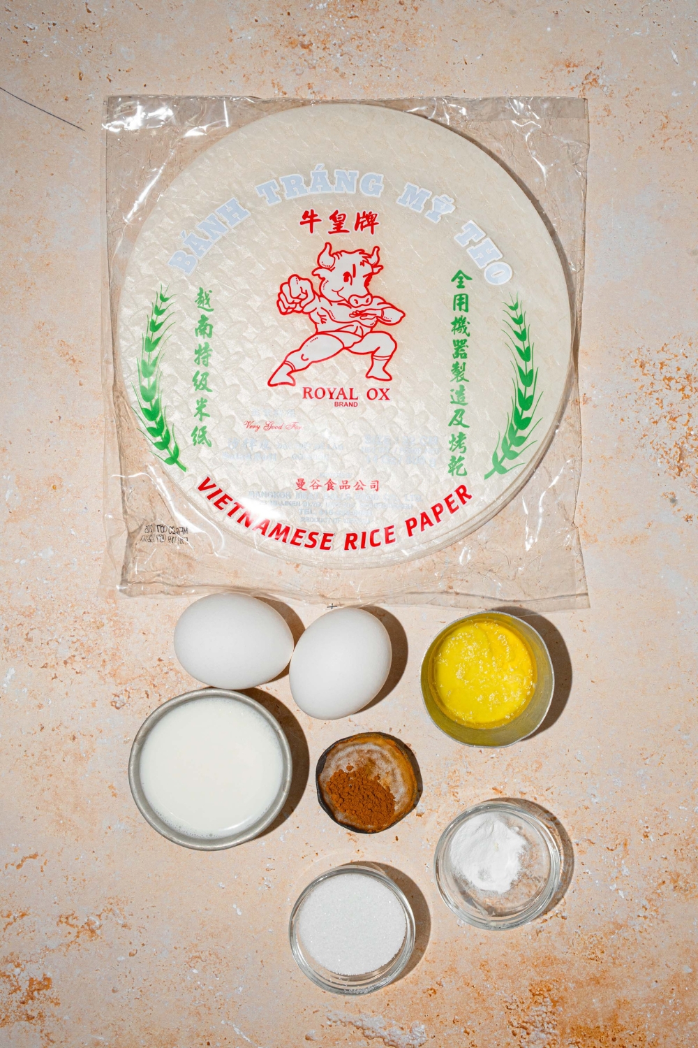 Several bowls in various sizes containing ingredients to make rice paper croissants including rice paper wrappers, egg, milk, sugar, vanilla, cinnamon, and baking powder.