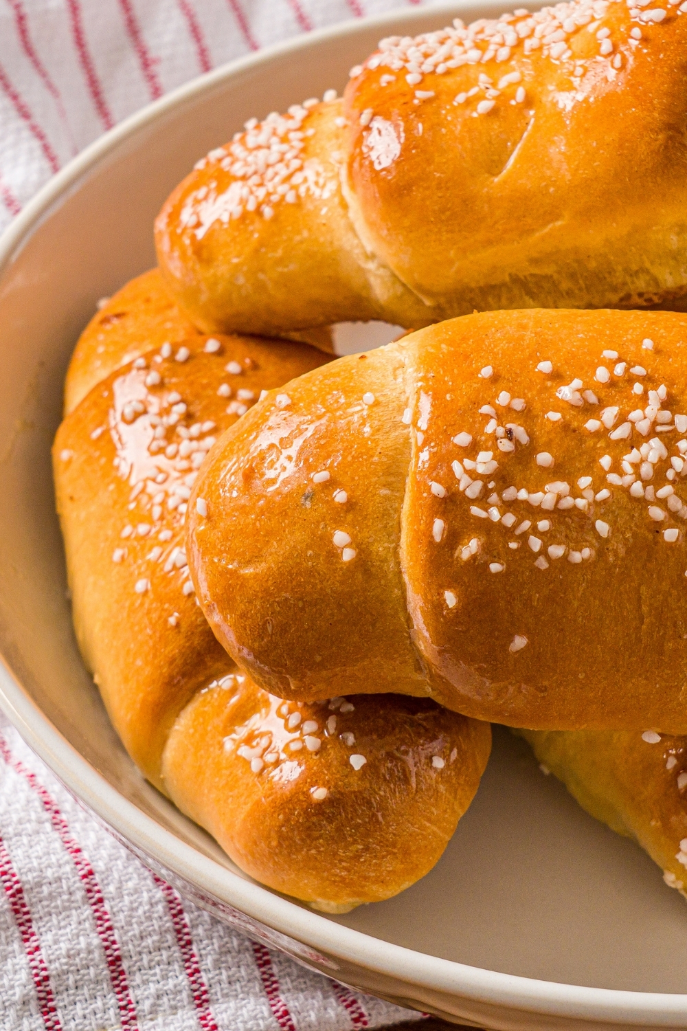 A white bowl with a pile of salt bread. The bowl is on a wooden counter with a red striped napkin.