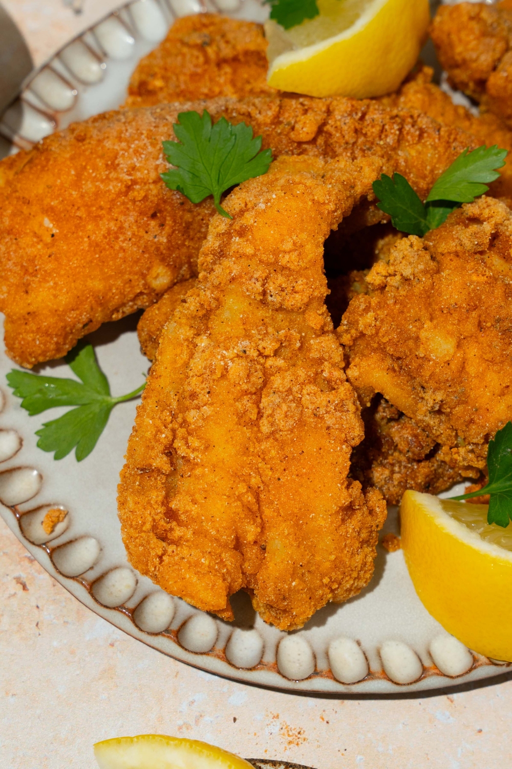 A white plate with several pieces of crispy Southern style fried fish garnished with fresh parsley and served with lemon.