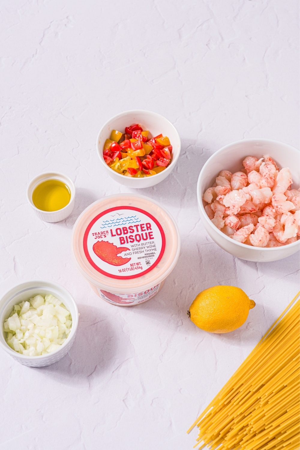 A marble counter with ingredients to make Trader Joe's lobster bisque pasta including lobster bisque, cooked shrimp, diced tomatoes, onion, oil, lemon, and pasta.